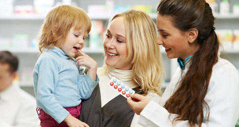 A female pharmacist stood with a mother and child giving them some medication